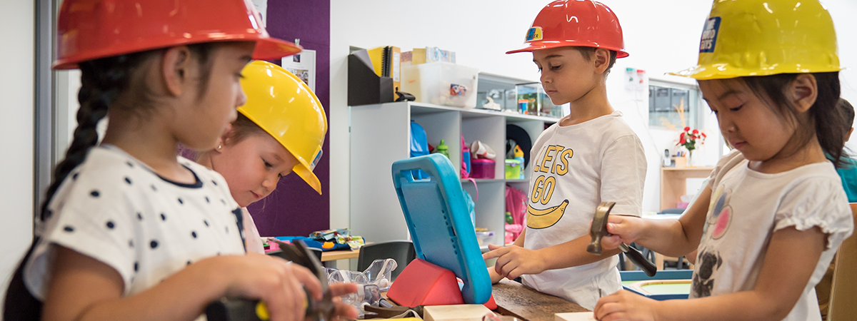 Four children wearing hard hats are taking part in an ELLA activity with an ipad in the centre of them.