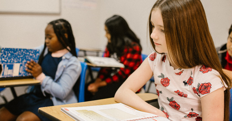 Young girl sits at school desk looking nervous.