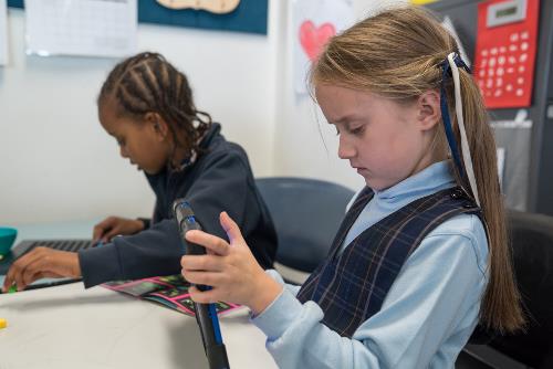 Girl in school uniform with two pigtails (ribbons in each hair) playing on tablet with face scrunched in concentration.