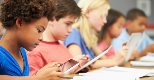 Students in class sitting in a row at desks using digital tablets