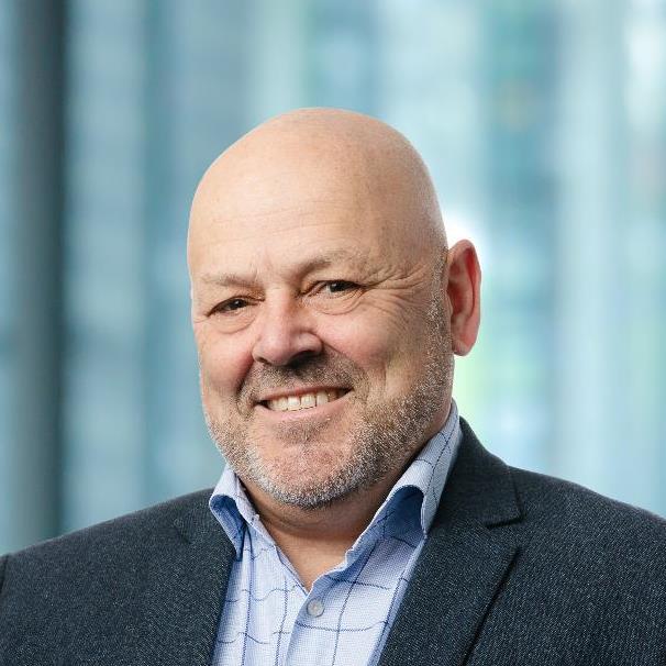 Portrait of Bret Morris wearing a blue shirt and jacket with the cityscape blurred in the background