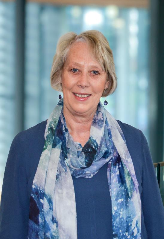 Portrait of Lynn Davie wearing a blue top and colourful blue scarf with the cityscape blurred in the background